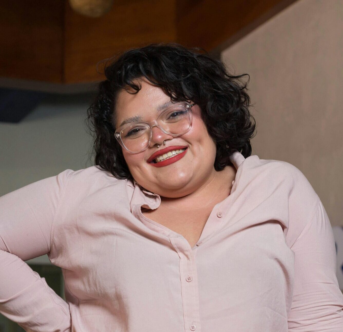 Plus-size woman smiling confidently with eyeglasses and pink shirt in an office.