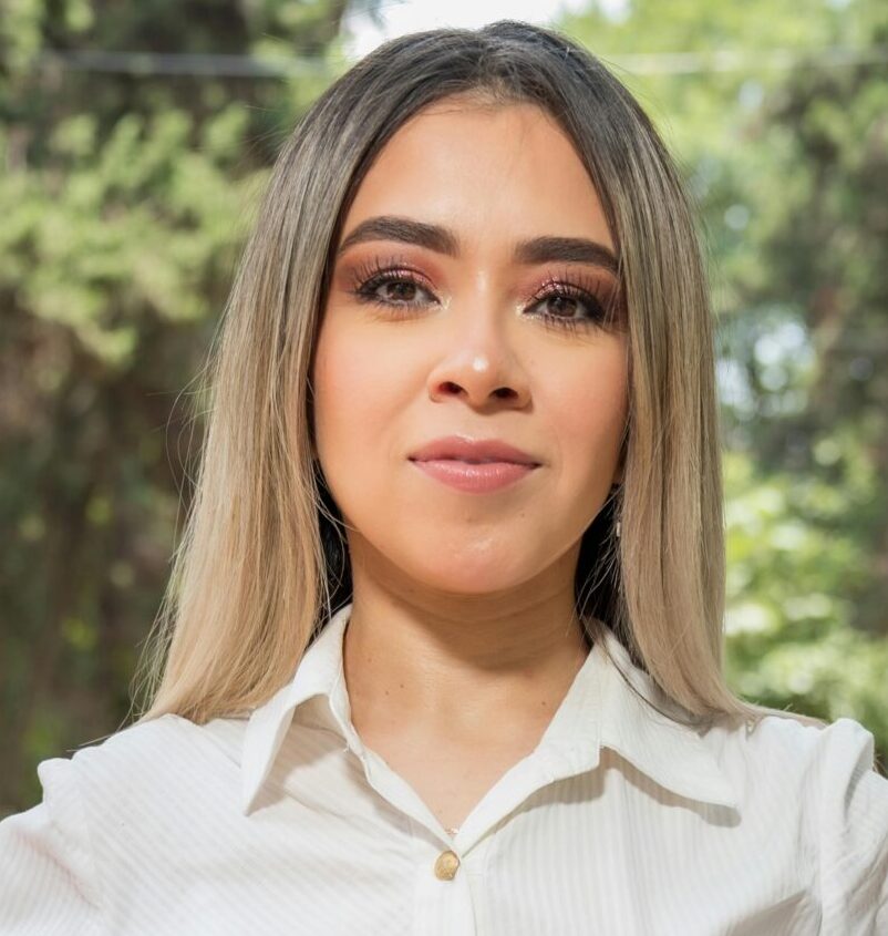 A confident woman poses outdoors in a park in Ciudad de México, wearing business casual attire.