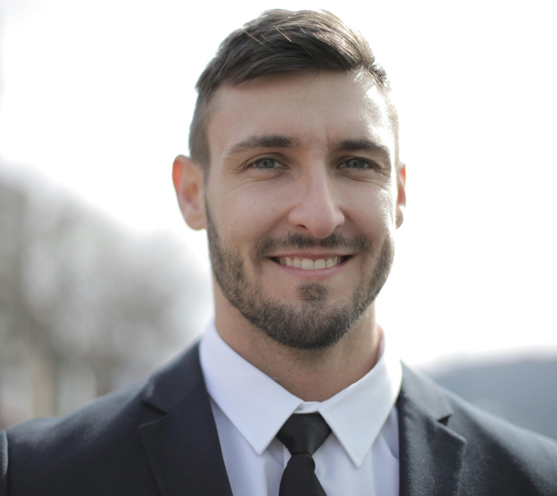 A smiling businessman in a suit standing outdoors with a bright expression.